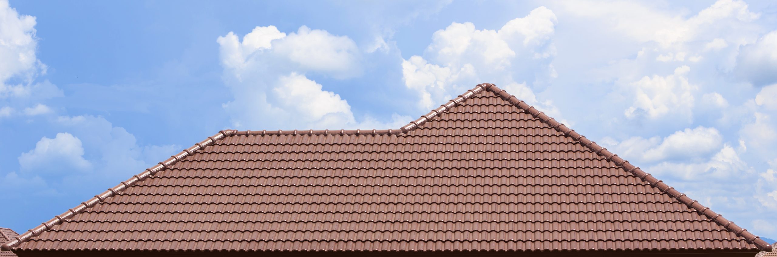 A house with a red-tiled roof against a blue sky with scattered white clouds. The roof's tiles are neatly arranged, and the sky provides a bright and clear backdrop.